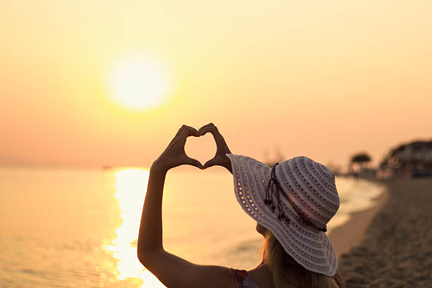 istock Girl on beach at sunrise making heart shape with hands 611101244