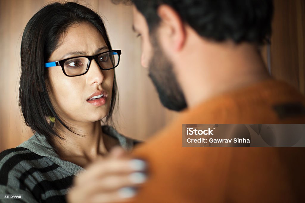 Happy Asian young man and woman talking face to face. Indoor over shoulder image of a serious Asian young woman with eyeglasses talking face to face with a young man. Two people, horizontal composition and selective focus. Discussion Stock Photo