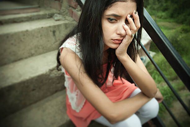 istock Sad Asian girl sitting on steps holding her head. 611105582