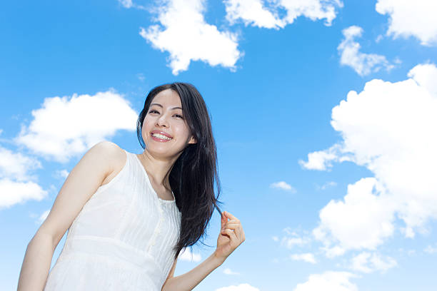 Portrait of a happy woman smiling and looking upwards under a bright and clear blue sky, feeling positive and confident. The image captures her radiant expression and the refreshing outdoor setting, embodying happiness, hope, and optimism—perfect for promoting positivity and well-being.