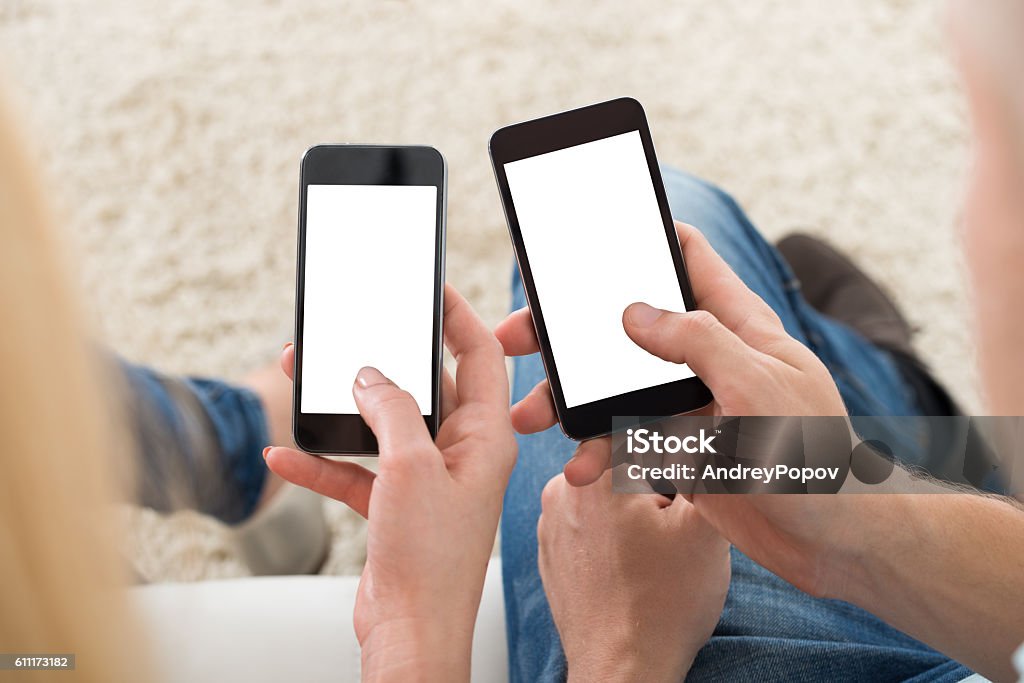 Couple Using Smart Phones At Home Cropped image of young couple using smart phones with blank screens at home Two People Stock Photo