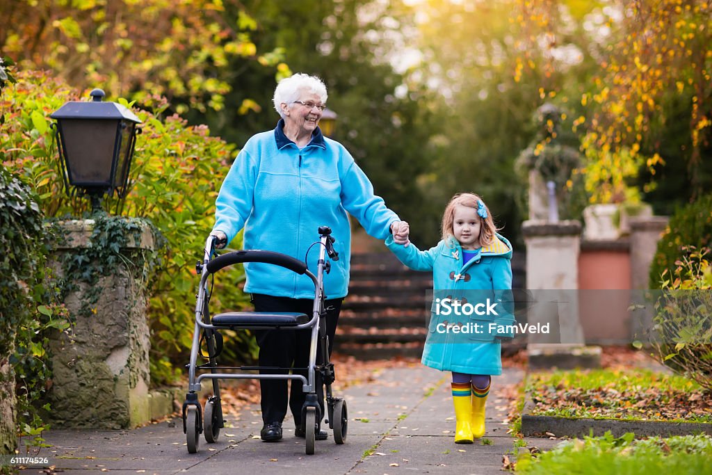 Senior lady with walker enjoying family visit in the park Happy senior lady with a walker or wheel chair and children. Grandmother and kids enjoying a walk in the park. Child supporting disabled grandparent. Family visit. Generations love and relationship. Rollator Stock Photo