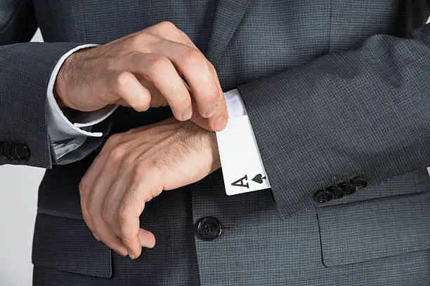 Midsection of businessman removing ace cards from sleeve in office