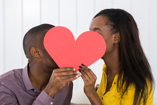 Close-up Of Young African Couple Hiding Behind Heart Shape