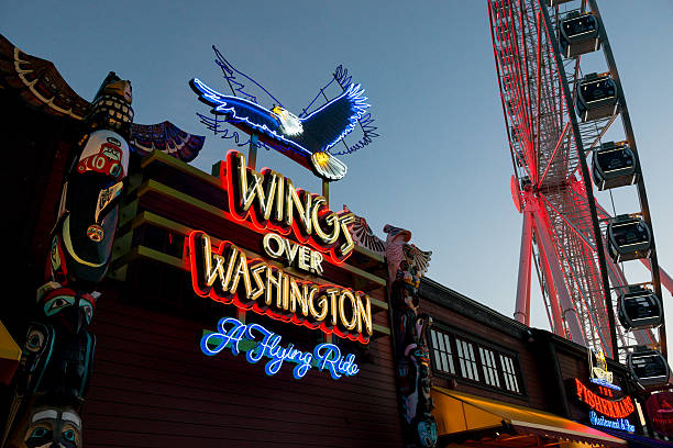 Miners Landing Seattle, USA - August 29, 2016: Neon at the Great Wheel and Wings of Washington on Pier 58 at Seattle Fishermans Wharf the famous tourist destination at sun set. pacific northwest totem poles stock pictures, royalty-free photos & images