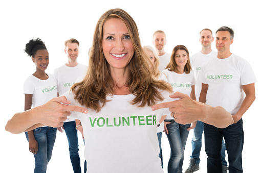 Portrait of happy woman showing volunteer text on tshirt with friends standing over white background