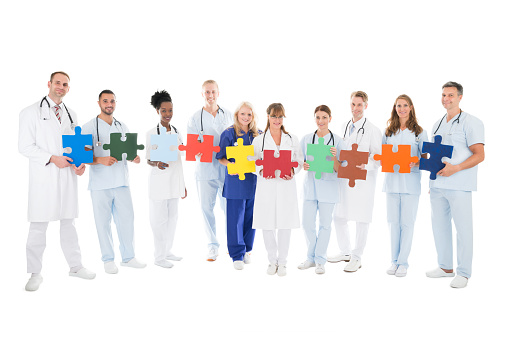 Full length portrait of confident medical team holding jigsaw pieces against white background