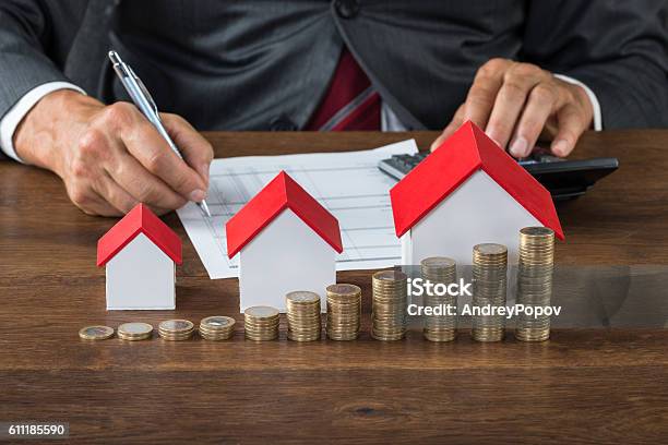Businessman Calculating Tax By House Models And Coins Stock Photo - Download Image Now