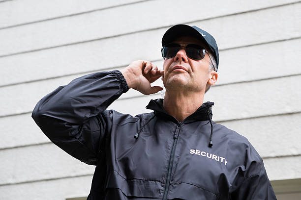 istock Confident Security Guard Listening To Earpiece Against Building 611185850