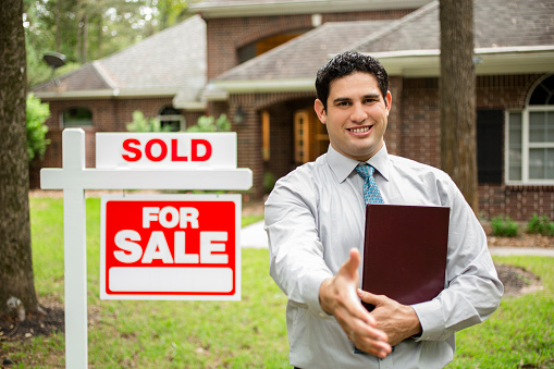 Real estate agent reaches for a handshake as he stands beside a 