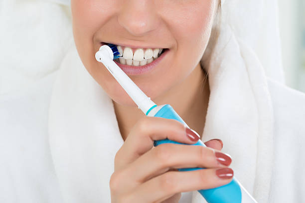 電気歯ブラシで歯を磨くバスローブの女性 - brushing teeth human teeth women cleaning ストックフォトと画像