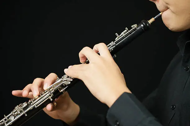 Close up of a person playing an oboe. Image shows the reed and the hand and finger positions. Studio shot on a black background.