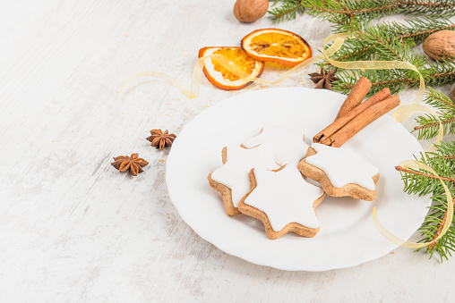 Close up of homemade butter nuts star shaped cookies with icing, pine, orange slices,cinnamon, anise, walnuts and golden ribbon over white wood background. Christmas decoration.