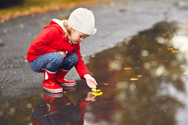 glückliches kind mädchen spielen mit herbstblättern in einer pfütze - puddle rain boot water stock-fotos und bilder
