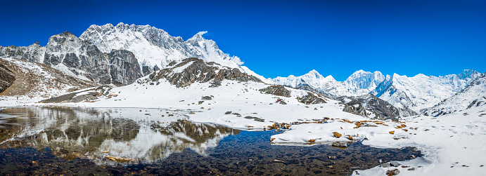 The jagged sawtooth ridge of Nuptse (7861m), the snow capped spire of Lhotse (8516m) and the massive summit pyramid of Makalu (8485m) eflecting in the tranquil blue waters of a high altitude lake deep in the picturesque Himalaya mountain wilderness of the Everest National Park, a UNESCO World Heritage Site.