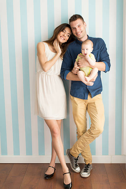 Young family with a baby standing by the wall