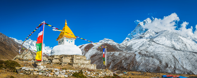 Traditional white-washed stupa and colourful Buddhist prayer flags fluttering in the thin mountain air above the Khumbu valley overlooked by Ama Dablam (6812m) deep in the remote Himalayan wilderness of the Sagarmatha National Park, a UNESCO World Heritage Site, Nepal.