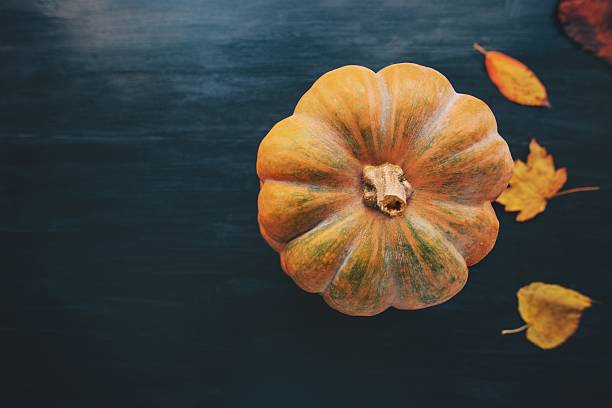 istock Pumpkin with fall yellow leaves on dark wooden background 611211872