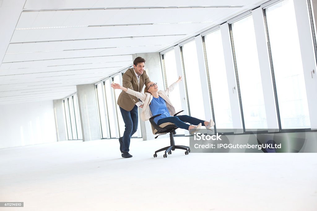 Young businessman pushing female colleague in chair at empty office Business Stock Photo