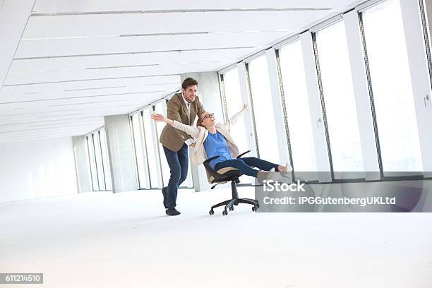 Young Businessman Pushing Female Colleague In Chair At Empty Office Stock Photo - Download Image Now