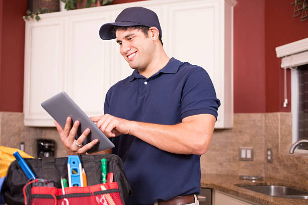 Repairman working inside customer's home. Hispanic repairman or blue collar/service industry worker makes service/house call inside customer's home kitchen. He has his tool box filled with work tools on counter as he uses his digital tablet.  Inspector, exterminator, electrician, plumber, repairmen.  He wears a navy blue uniform. inspector stock pictures, royalty-free photos & images