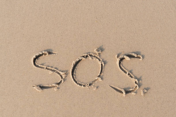 "SOS" message written on sand beach stock photo