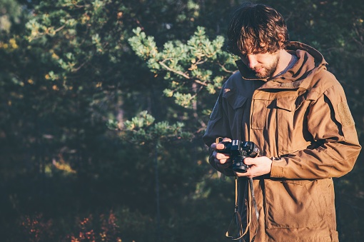 Young Man traveler with retro photo camera walking in forest Fashion Travel Lifestyle outdoor