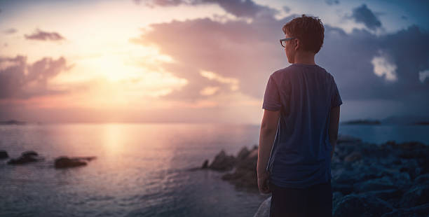 A boy standing near the sea and enjoying the magnificent nature and sunset. Stock photo.