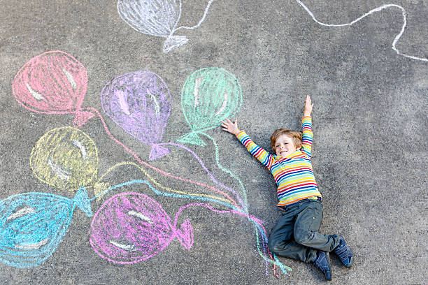 istock Kid boy having fun with colorful balloons drawing with chalks 611293202