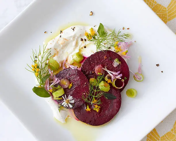 An artfully plated beet salad dish on a white square plate.