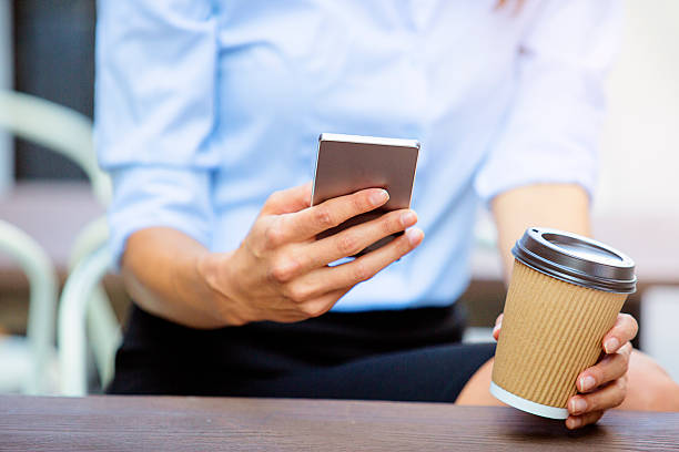 istock Using smartphone and holding coffee to go close up 611296384