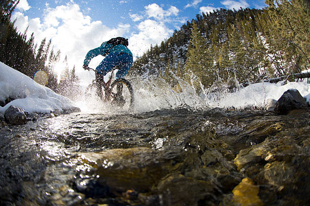 Winter Mountain Bike Creek Crossing A man rides through a creek during a winter mountain bike adventure in the Rocky Mountains of Canada. mountain bike stock pictures, royalty-free photos & images