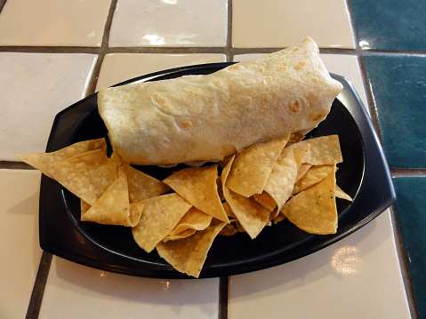 Burrito and Chips on a Plastic plate on a multi-tiled table.