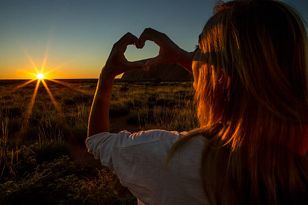 istock Silhouette of woman making heart shape finger frame on sunset 611310356