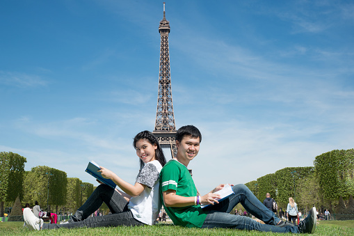 Asian couple student reading book together at outdoors park near Eiffel Tower in Paris, France. Abroad study in Paris, France.