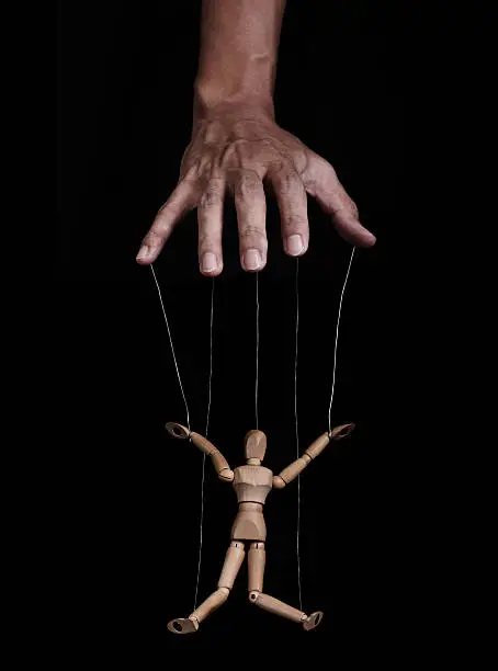 Hand controlling wooden puppet figure, low key images, on black background