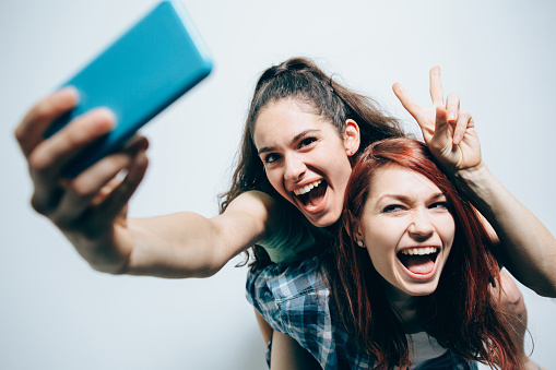 Studio shot of two friends who are taking a selfie on a piggyback