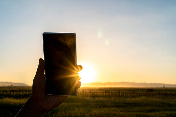 istock hand holding smart phone on pasture at sunset 611333802