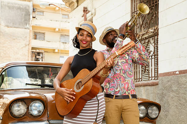 Cuban musicians outdoors, Havana, Cuba A beautiful young Cuban woman with a guitar and a musician with a trumpet standing on the street next to an old car, a woman smiling, looking at camera, Havana, Cuba, 50 megapixel image. cuban ethnicity stock pictures, royalty-free photos & images