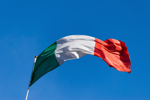 National Italian flag with pole flowing in the wind on a clear blue sky.