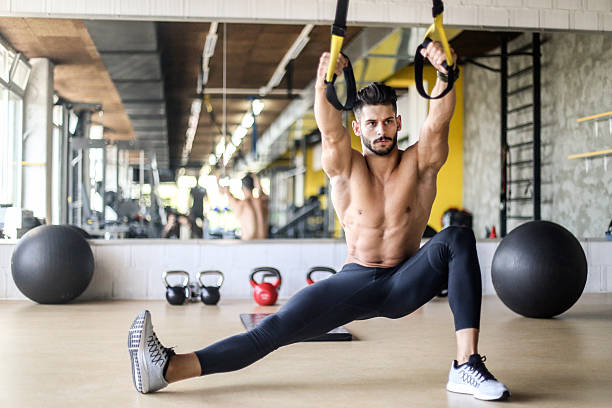 Suspension exercise with straps Young muscular man exercising with TRX hanging suspension fitness straps. About 20 years old Caucasian shirtless man. suspension training stock pictures, royalty-free photos & images