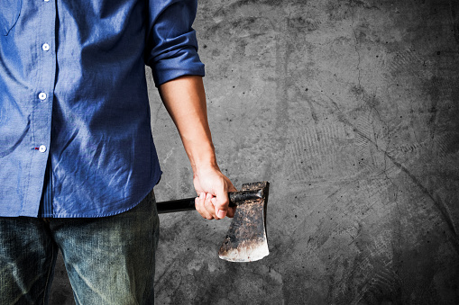 A guy holding old rusty axe, close up front view, on dark concrete texture background with copy space