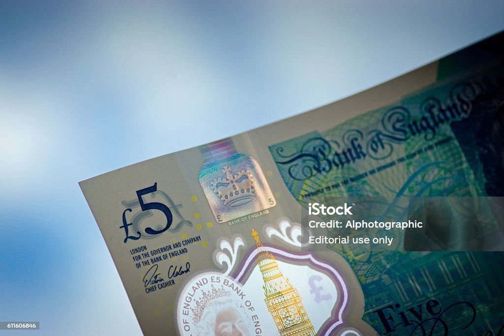 New 5 pound note Huntingdon, UK - September 30, 2016: The new UK 5 pound note with the logo prominent against an out of focus blue sky. The image was taken in a garden with the note held up against the sky. The note is one of the new plastic ones and this image concentrates on corner that shows the £5 symbol.. 2016 Stock Photo