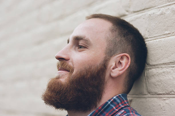 portrait of a dreaming man with a beard in front of the white brick wall