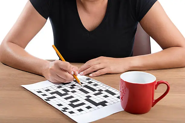 Adult woman solving crossword puzzle with yellow pencil.    