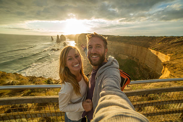 Cute couple take selfie at Twelve Apostles, Australia Young couple take a selfie portrait at sunset by the Twelve Apostles sea rocks on the Great Ocean Road in Victoria's state of Australia. twelve apostles sea rocks victoria australia stock pictures, royalty-free photos & images