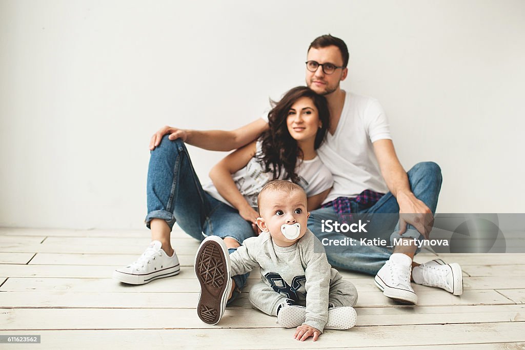 Young hipster father, mother and baby boy on wooden floor Young hipster father, mother and cute baby boy sitting on rustic wooden floor over white background Family Stock Photo