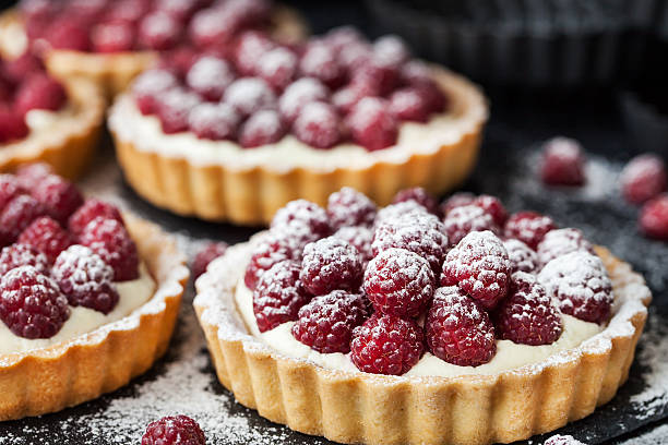 Delicious raspberry mini tarts on dark background Delicious raspberry mini tarts (tartlets) with whipped cream on dark background baked pastry item stock pictures, royalty-free photos & images