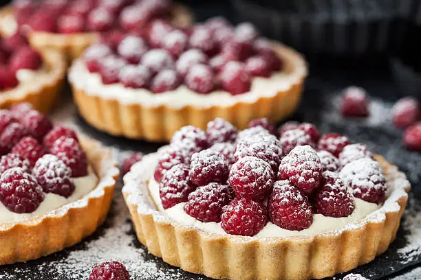 Photo of Delicious raspberry mini tarts on dark background
