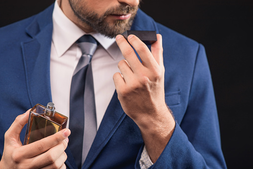 Self-confident young businessman is enjoying smell of masculine perfume. He is standing and holding bottle. Isolated